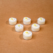 Six white tealight candles with daisy flower tops on a brown background